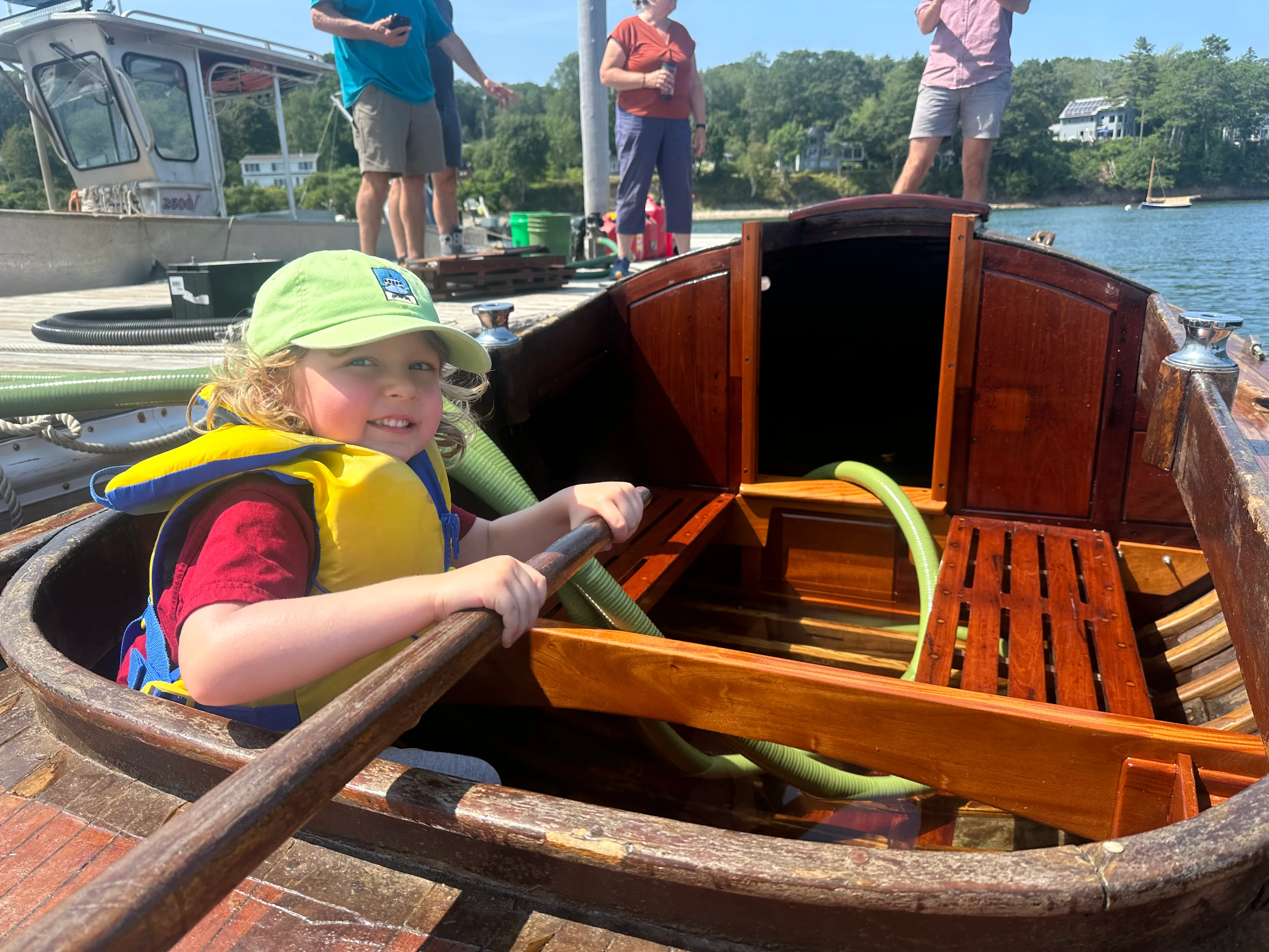 A young child in a yellow life jacket sitting in the cockpit, smiling