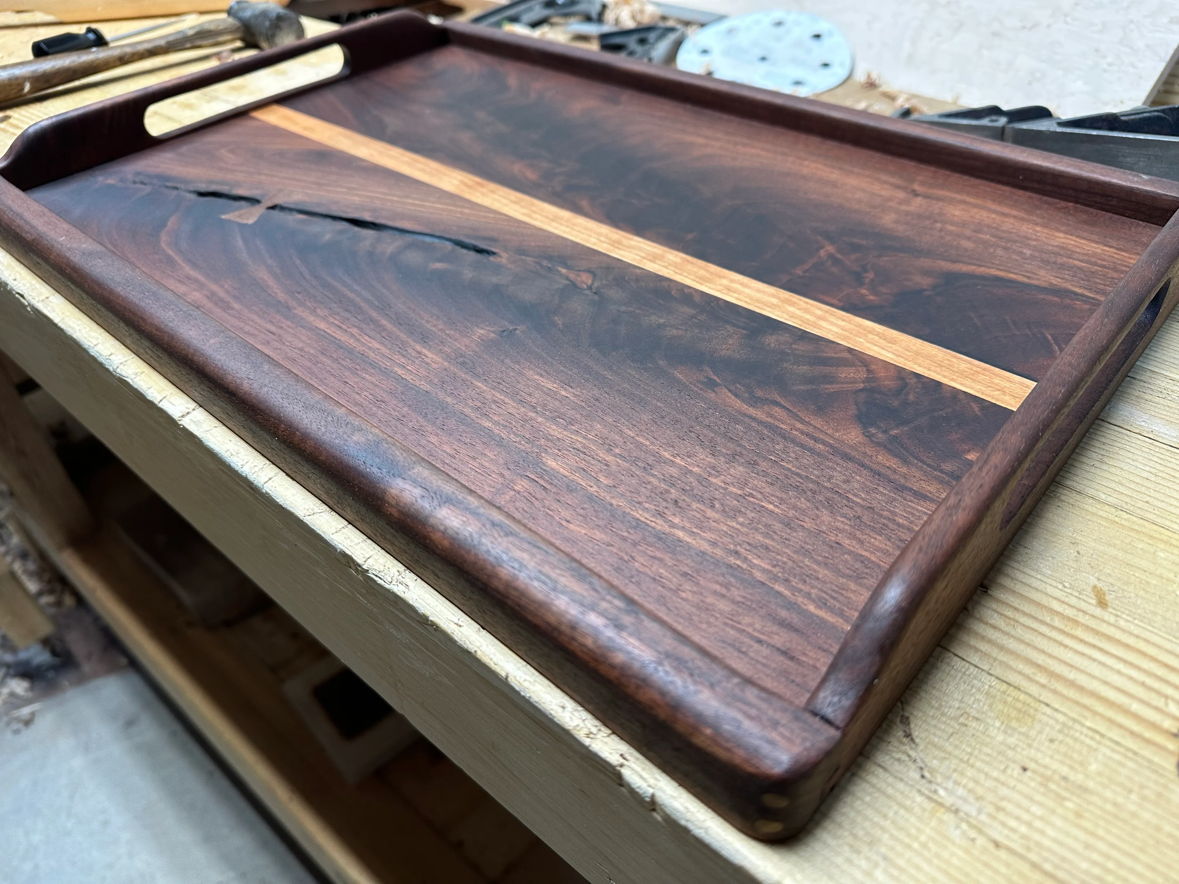 Finished walnut tray at an angle showing figured panel, maple strip, bow tie, and walnut frame