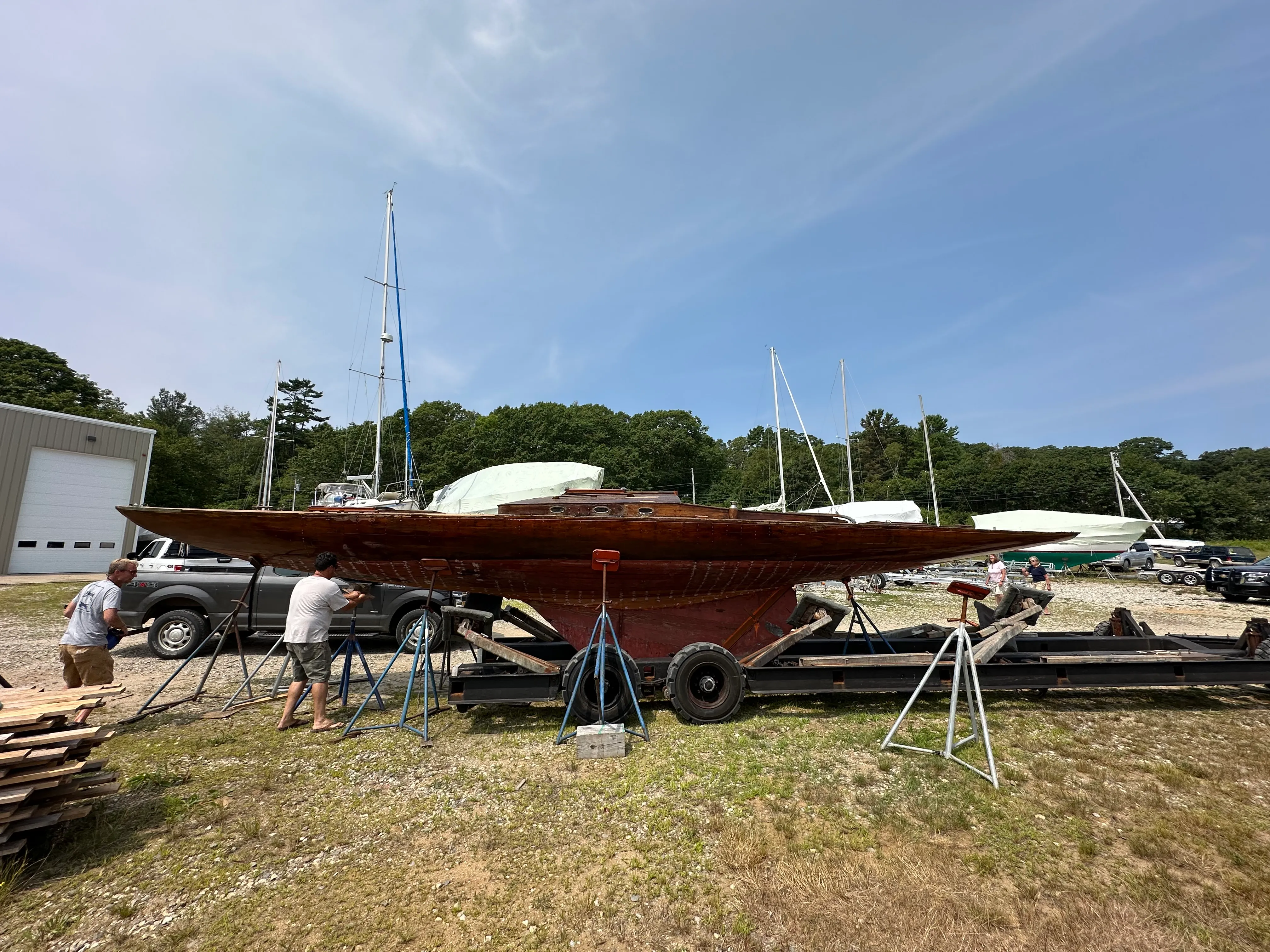 The boat being set up on jack stands at the boatyard, two people positioning stands