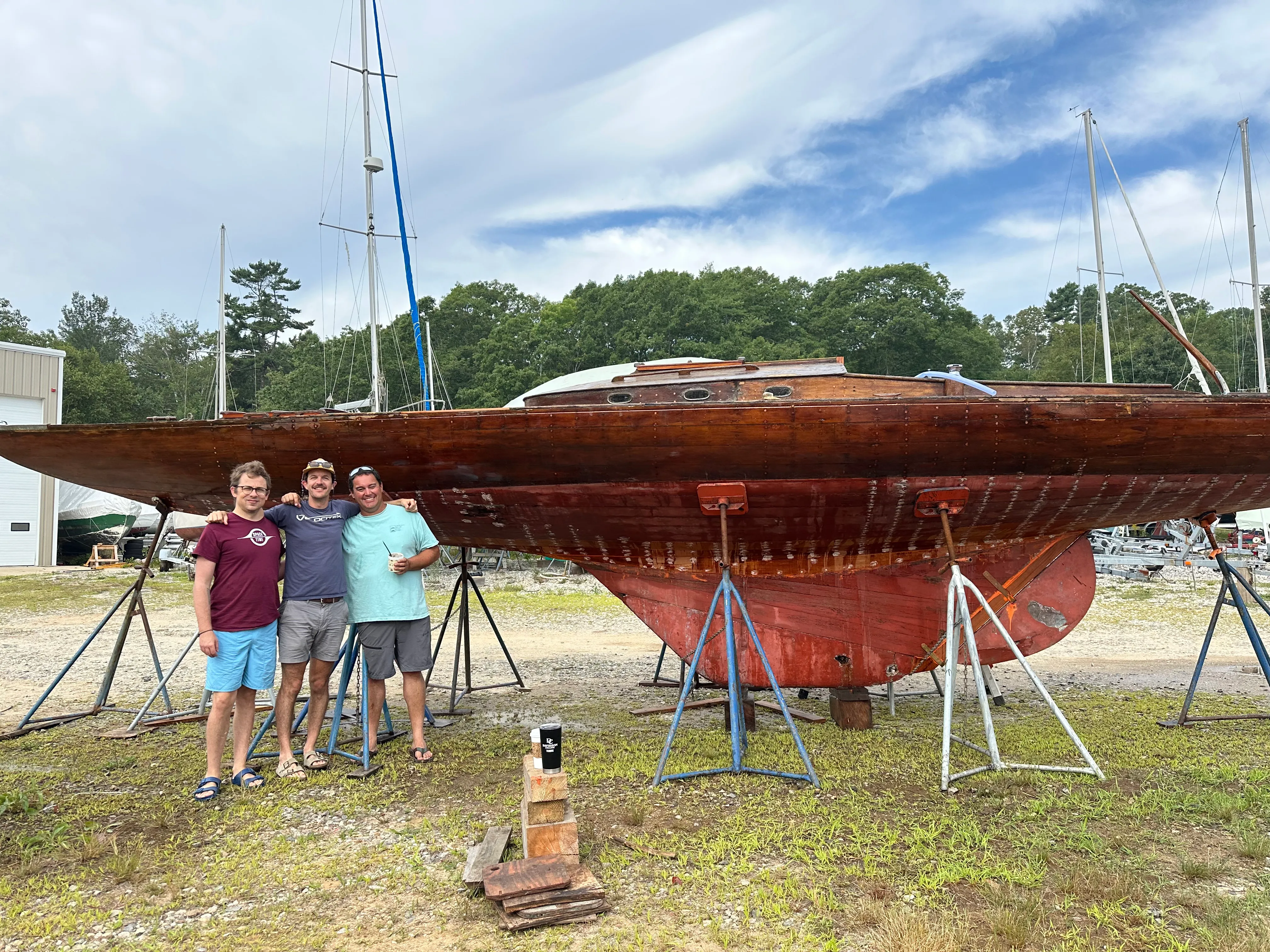 Three people posing in front of the sailboat on jack stands at the boatyard