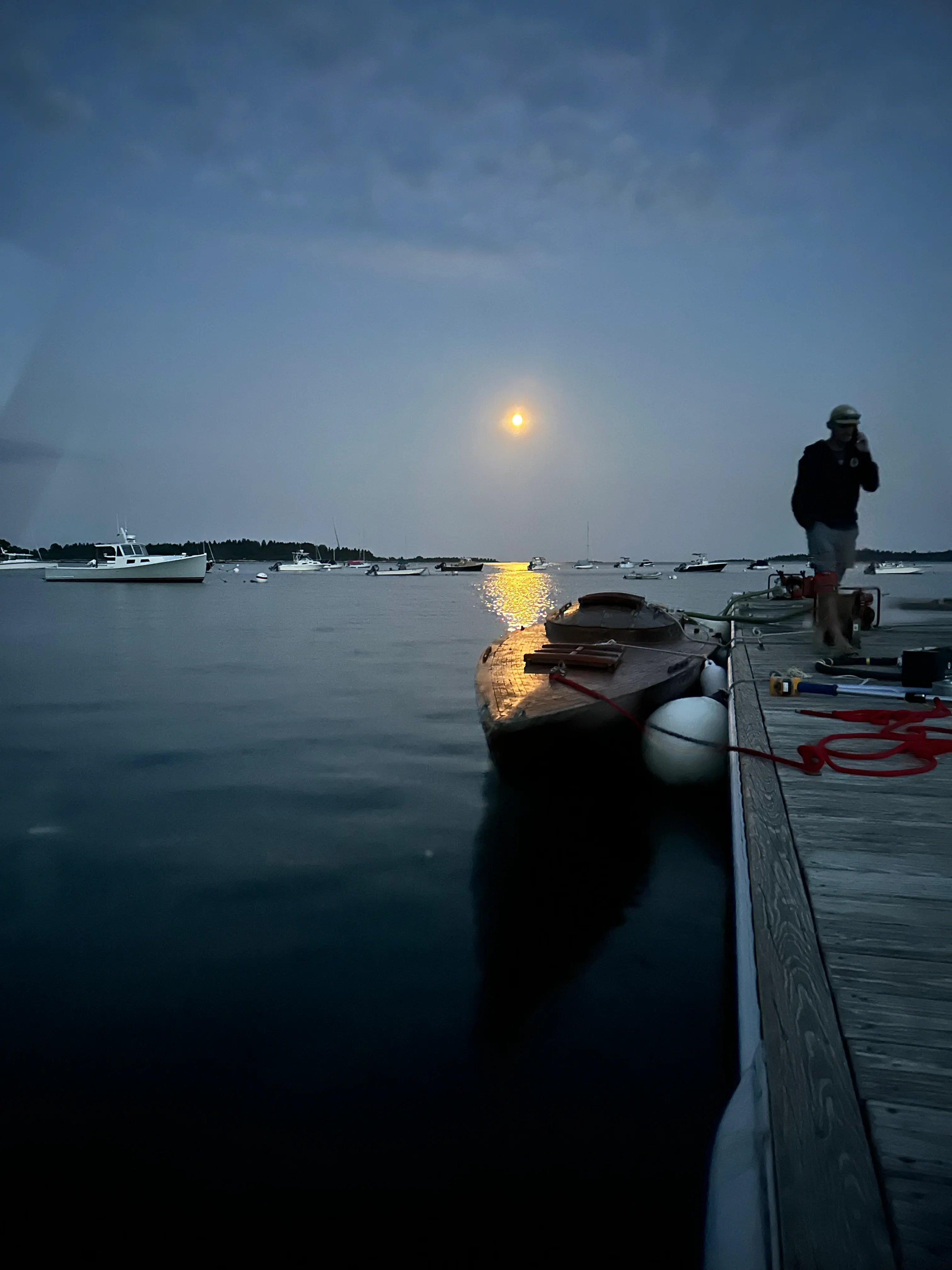 Silhouette of a person standing on the dock at dusk with the boat and warm light over the harbor