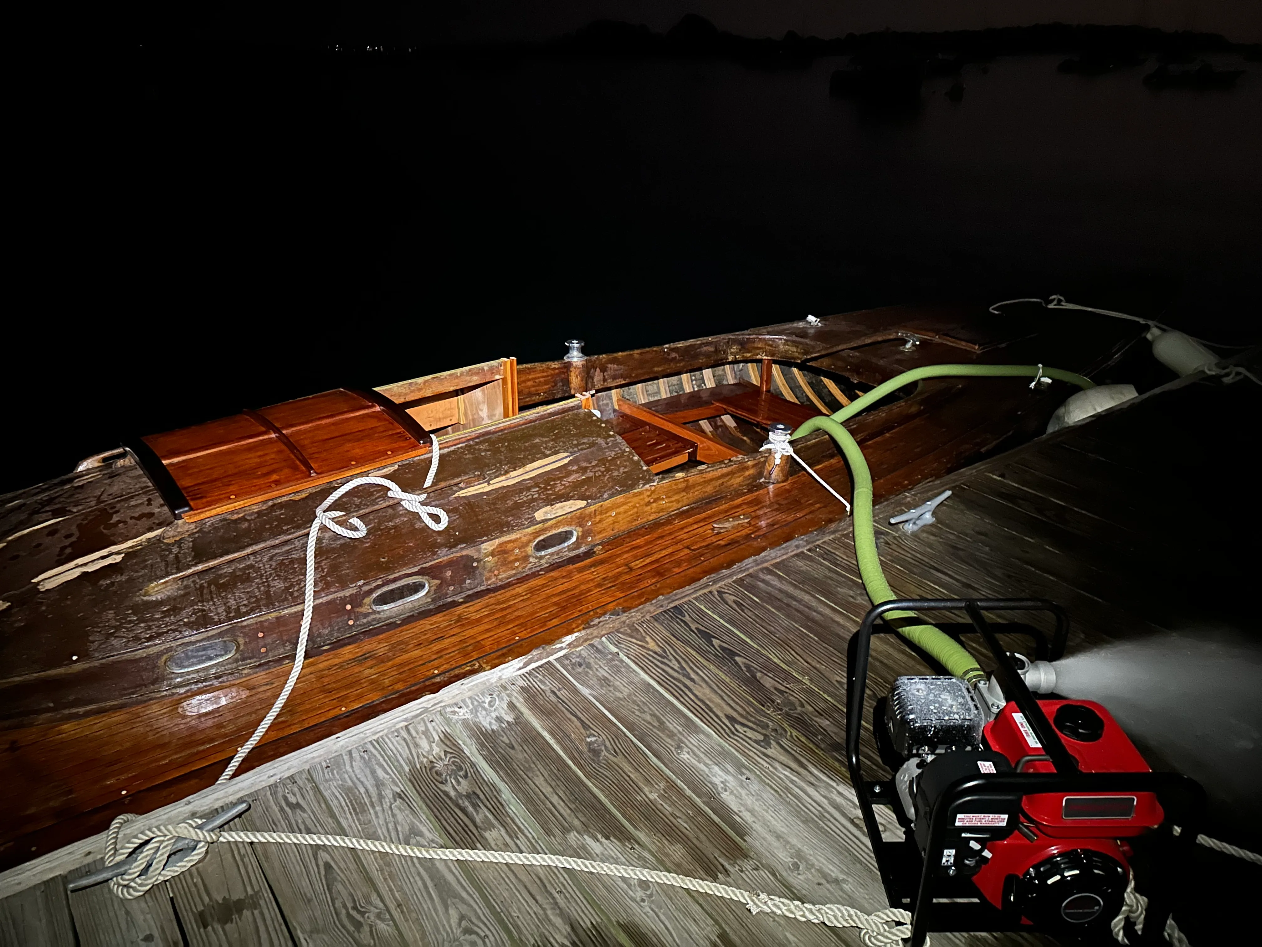 Nighttime overhead view from the dock showing a red gas-powered pump on the dock with its hose running into the cockpit