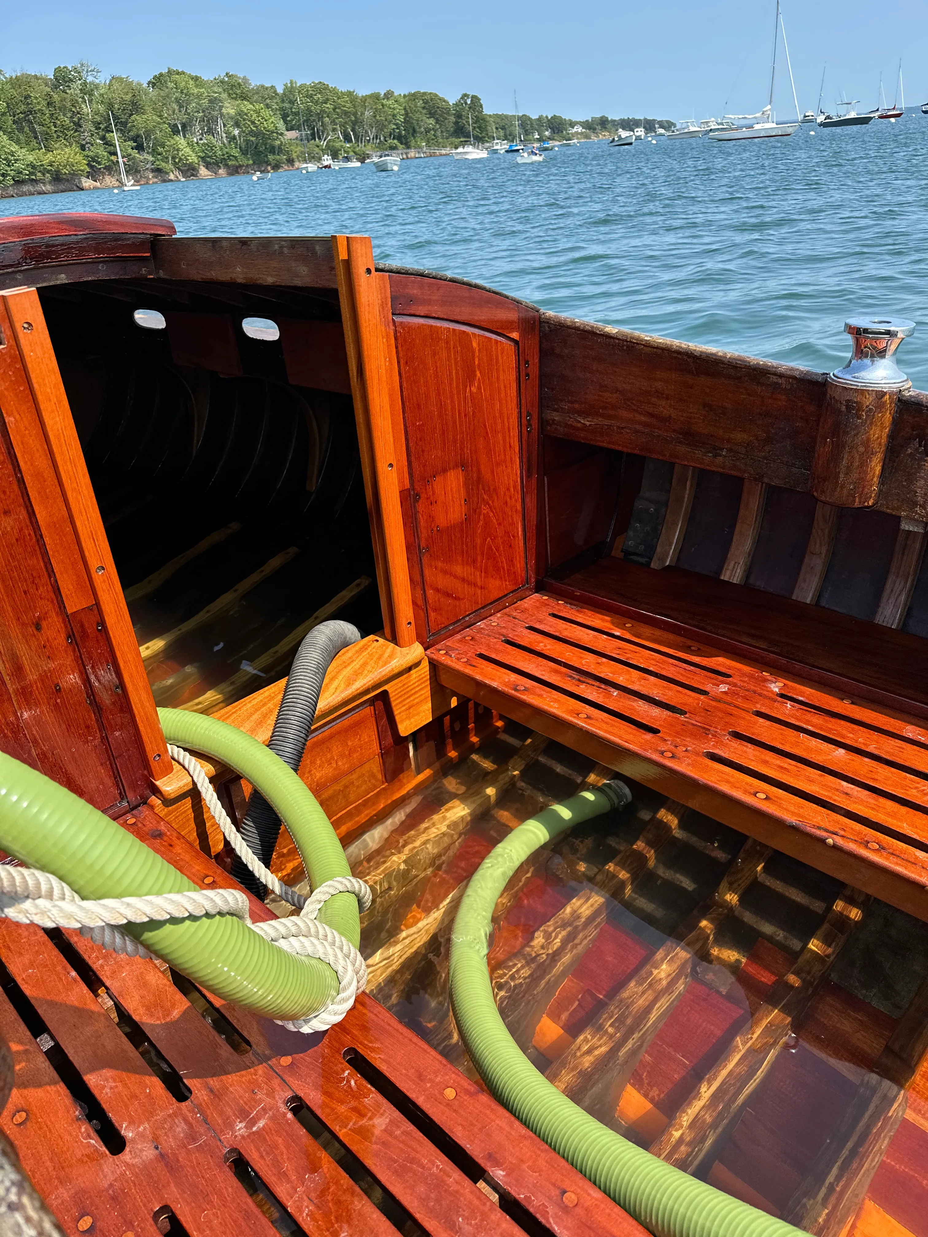 Cockpit interior showing varnished wood and a green pump hose running into the bilge