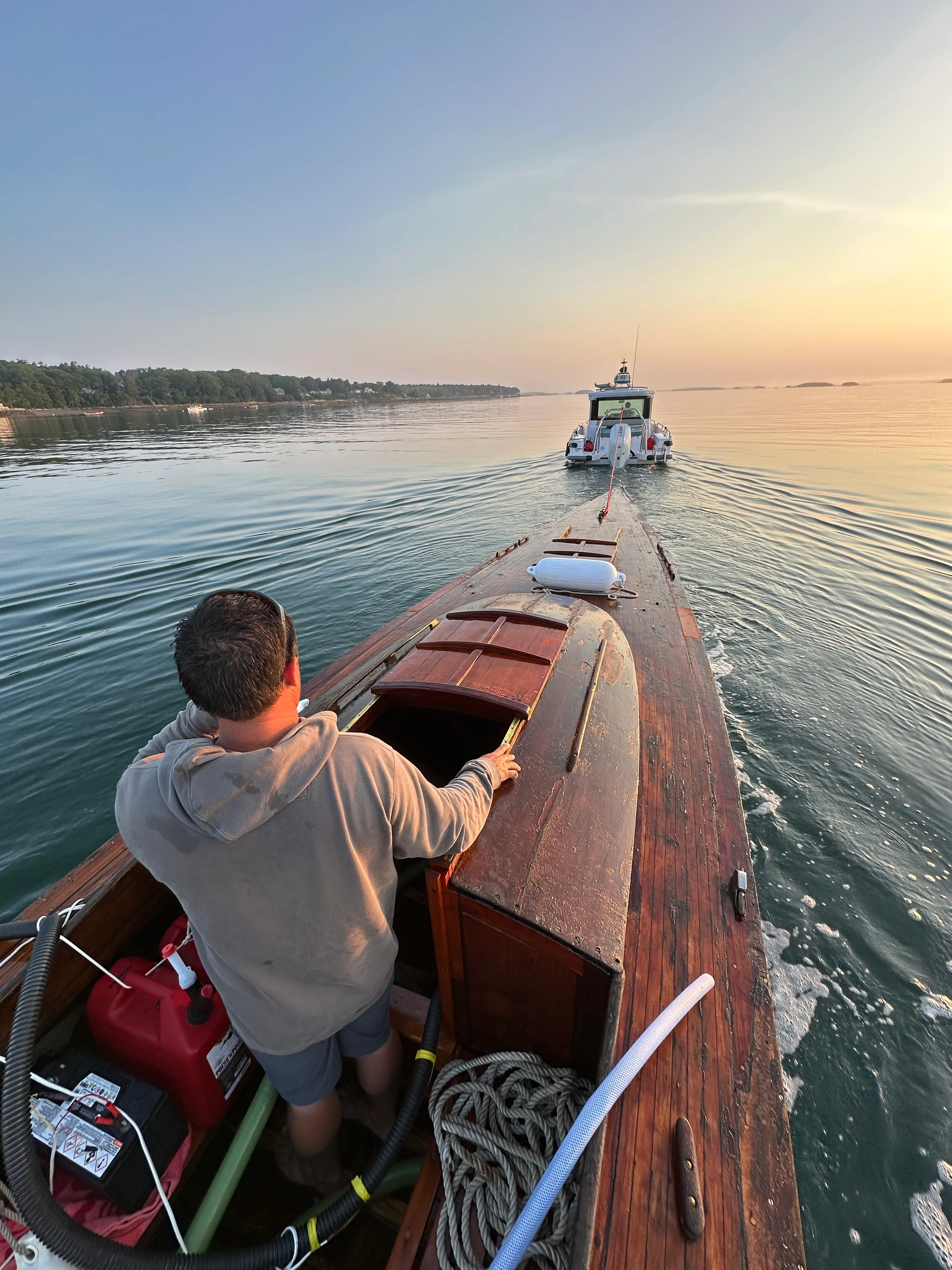 Person sitting in the cockpit at golden hour, looking forward at the tow boat, with pump equipment visible