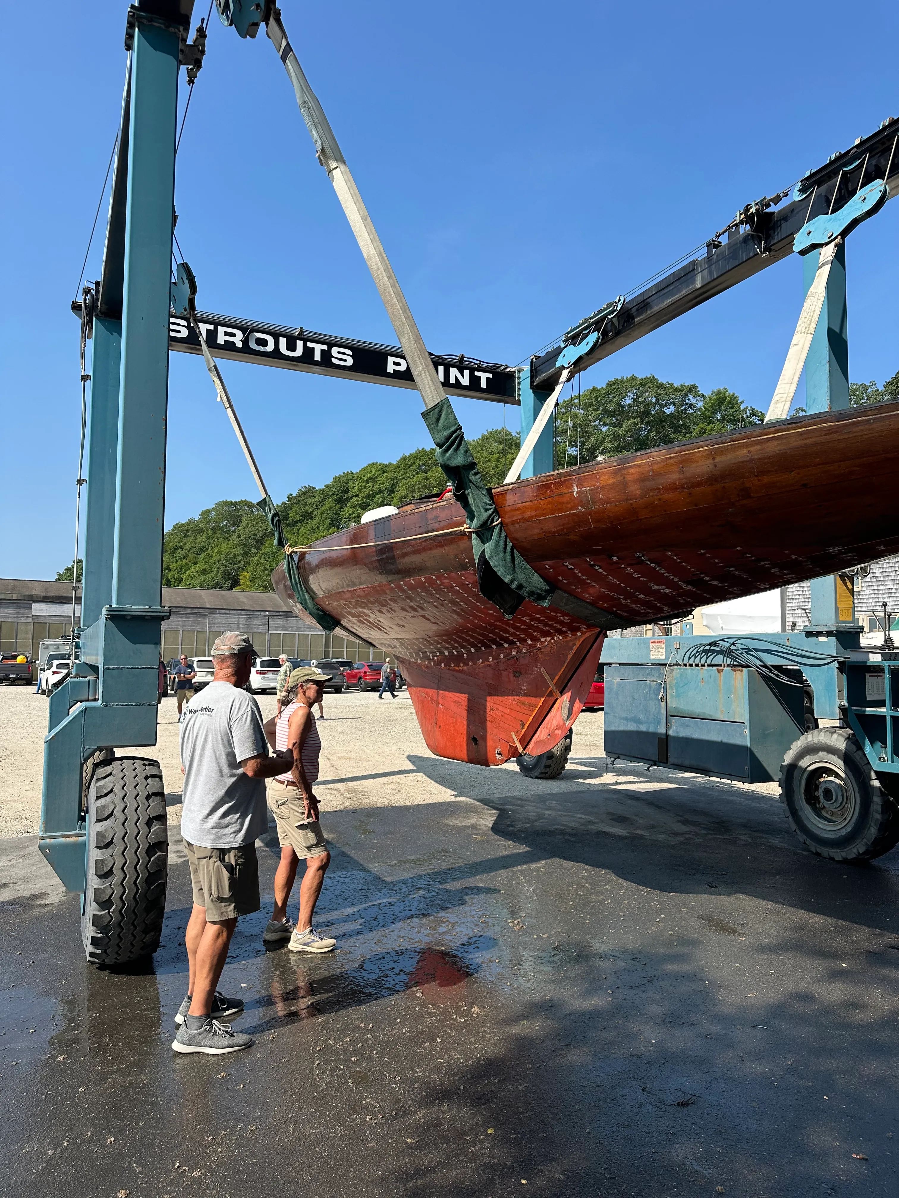 Two people standing beneath the sailboat hanging in the Travelift, showing the scale of the hull