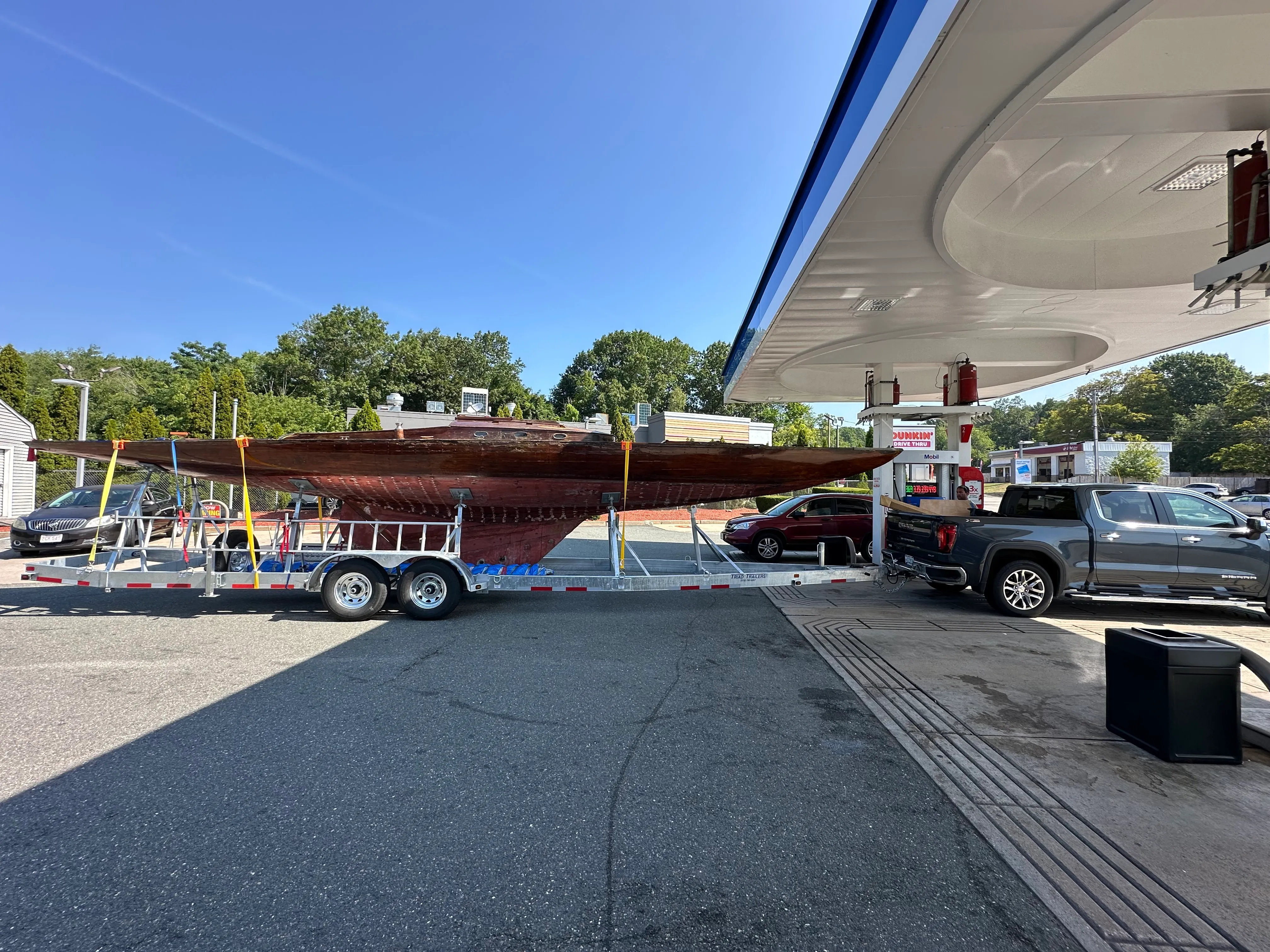 The sailboat on a trailer stopped at a gas station, showing the length of the hull