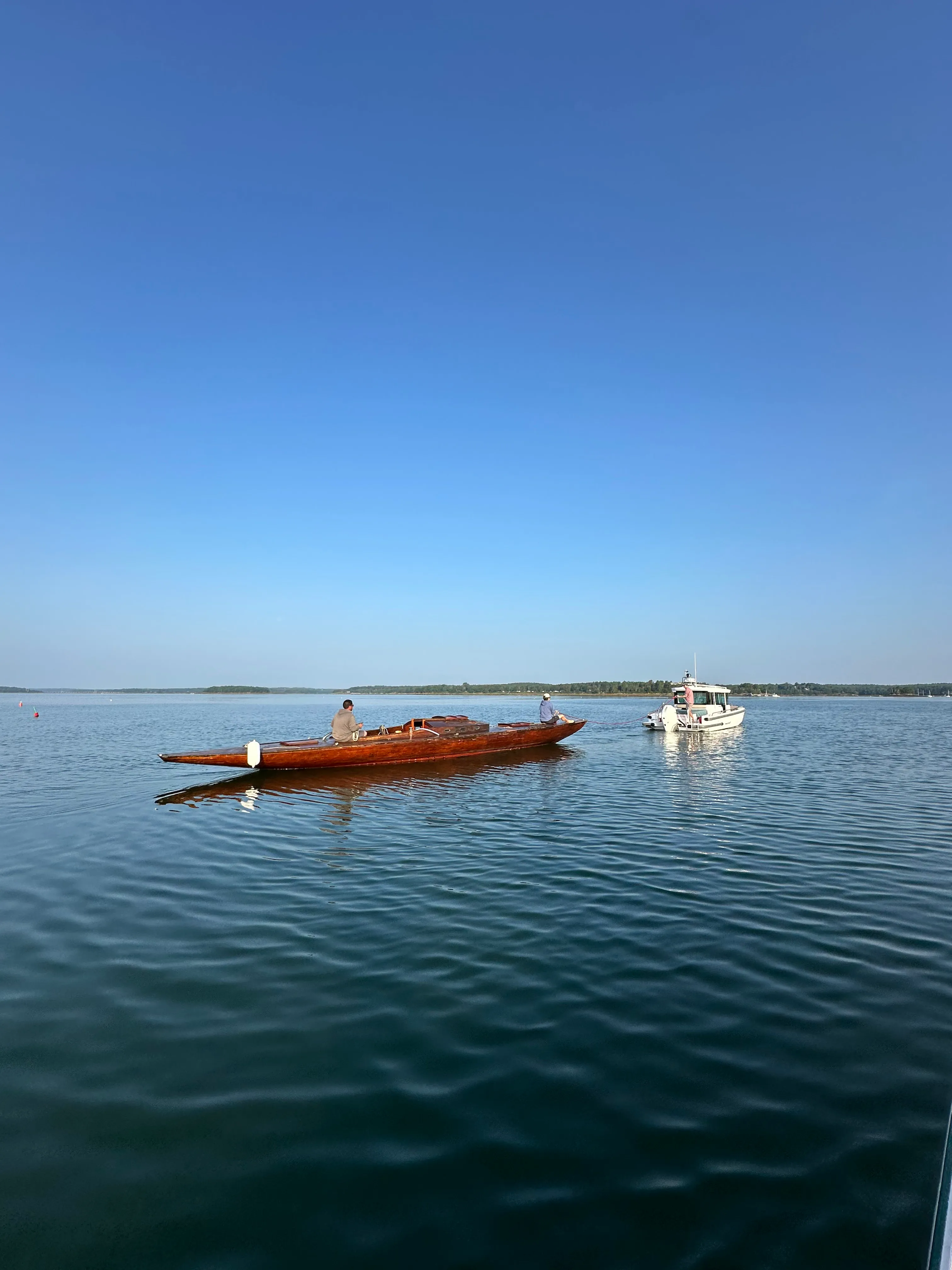 Distant view of the sailboat being towed across open water on a calm day