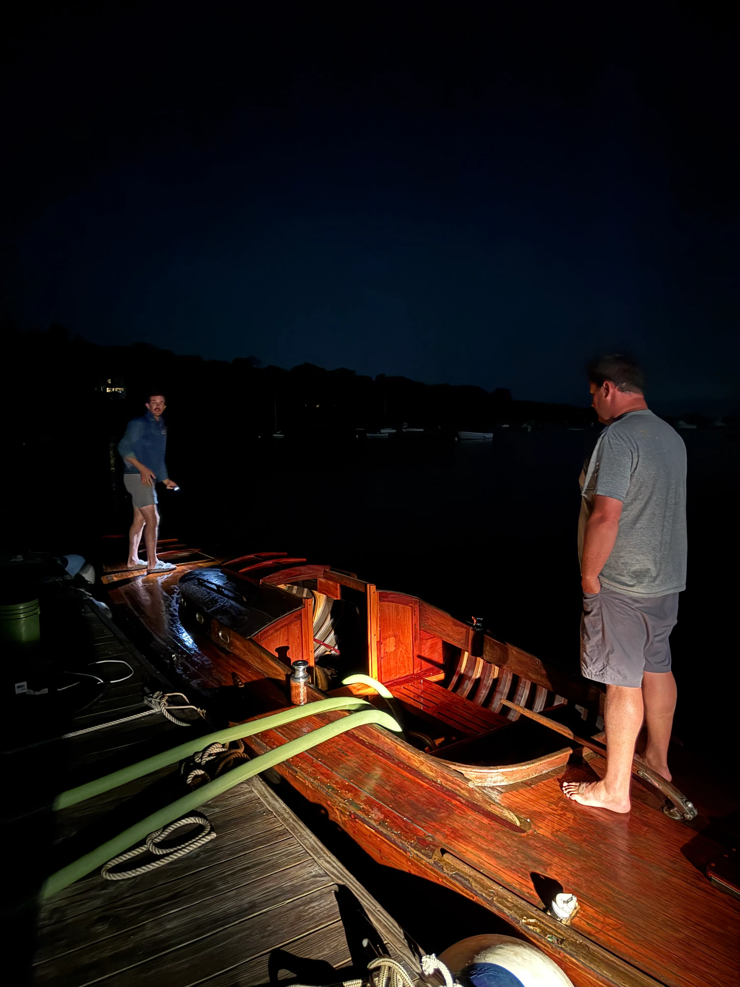 Two people aboard the boat at night, illuminated by a light showing the varnished interior