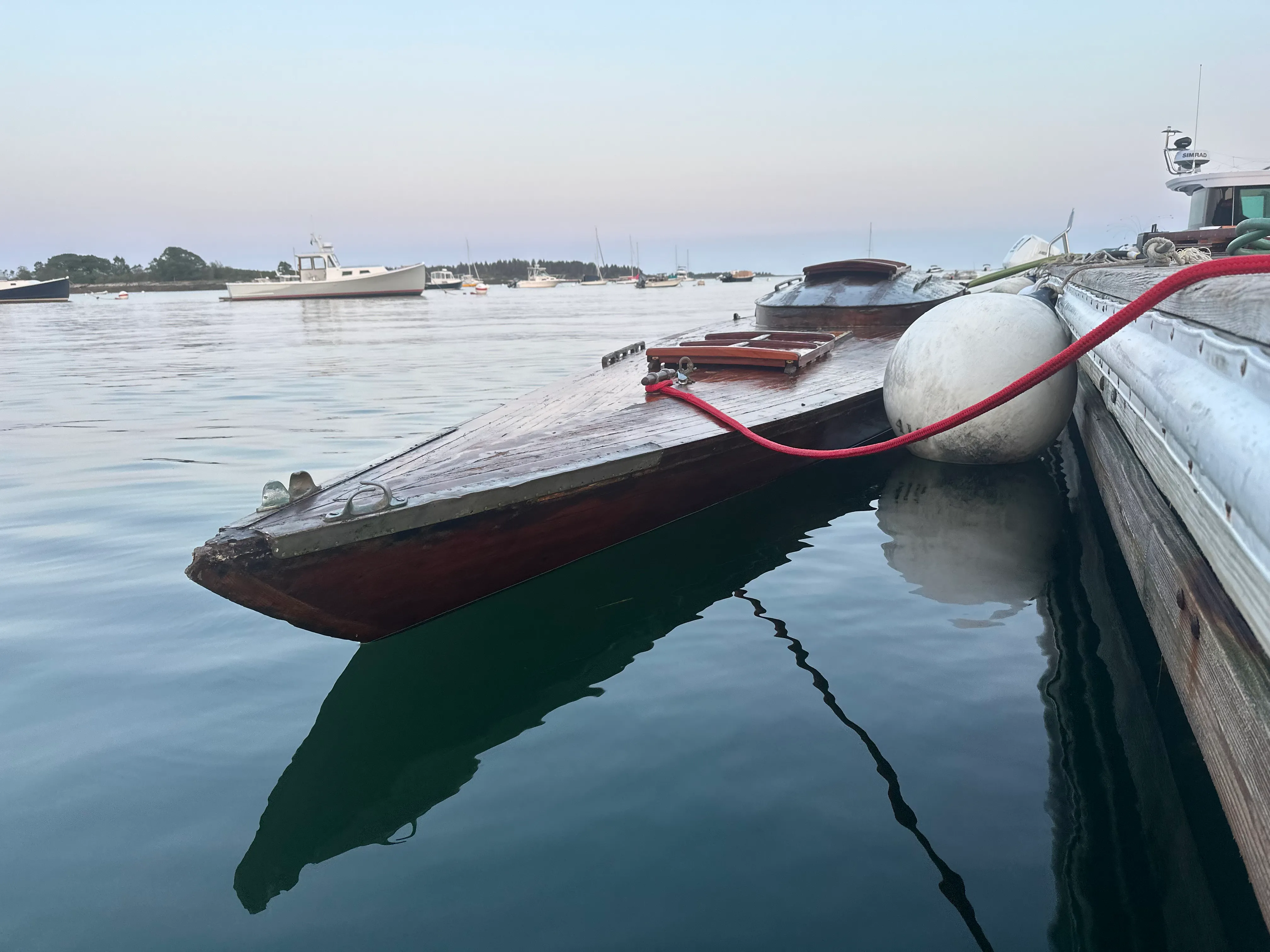 Low-angle view of the hull at the waterline at dusk, with glassy calm water and harbor reflections